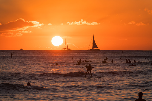 Oahu, USA - Nov 4, 2021: Swimmers and Surfers off Waikiki Queens Beach as the sun sets.
