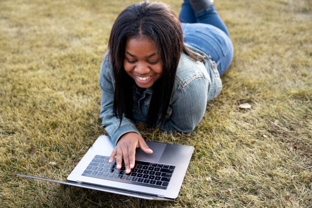 Happy Young African American Woman, College Student, Looking At A Laptop Computer, Taking Time To Study On a Lawn stock photo