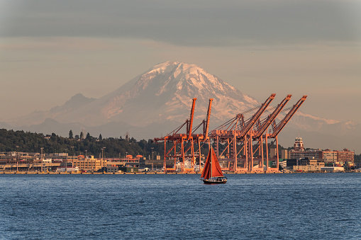 Seattle, USA - Aug 13, 2019: A ferry and sailboat on Elliott bay late in the day with Mount Rainer and the ports in background.