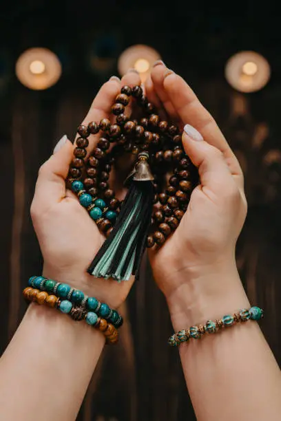 Photo of Woman holding wooden mala beads strand, used during meditations. Lady sits among candles. Spirituality, religion, God concept.
