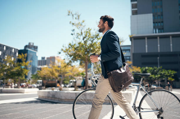 shot of a young businessman traveling through the city with his bicycle - cycling imagens e fotografias de stock