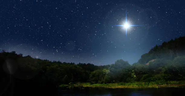 Photo of Bright star indicates the Nativity of Jesus Christ in the starry sky. Fog is rising over the night forest.