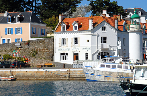 Commercial quayside and lighthouse, Sauzon harbour, La Belle Ile, Morbihan, France. Sauzon is one of the main ports on the island and a tourist attraction with its beautiful architecture and tidal basin marina that attracts recreational sailors and fishing boats alike