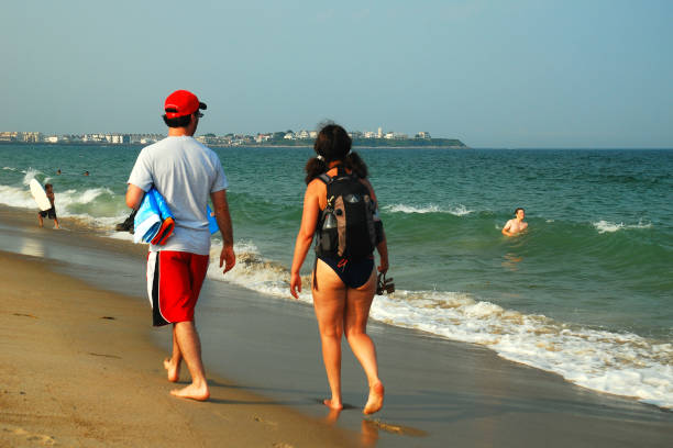 Hampton Beach, NH, USA July 15 A young adult couple walks along the sands at the water's edge on a sunny summer vacation day in Hampton  Beach, New Hampshire