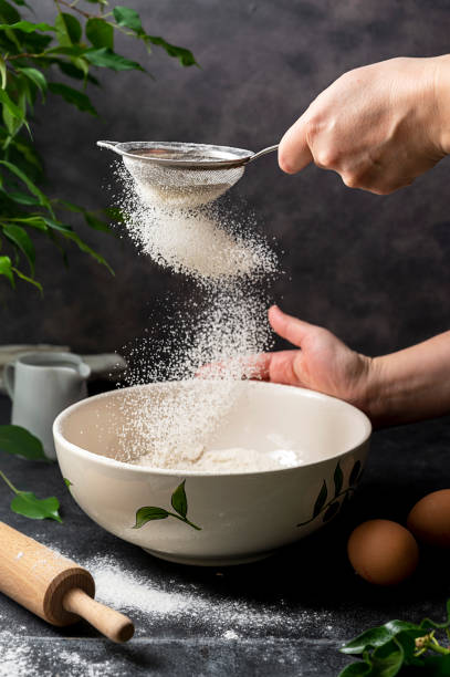 istock Woman's hand sifting flour through sieve. Selective focus. Baking, cooking, pastry abstract concept. Dark background 1368060314