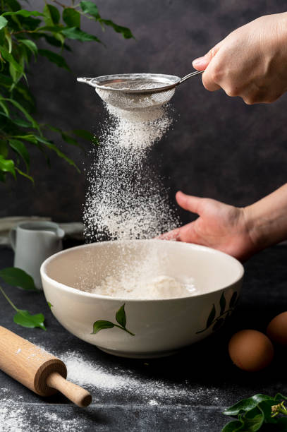 istock Woman's hand sifting flour through sieve. Selective focus. Baking, cooking, pastry abstract concept. Dark background 1368060315