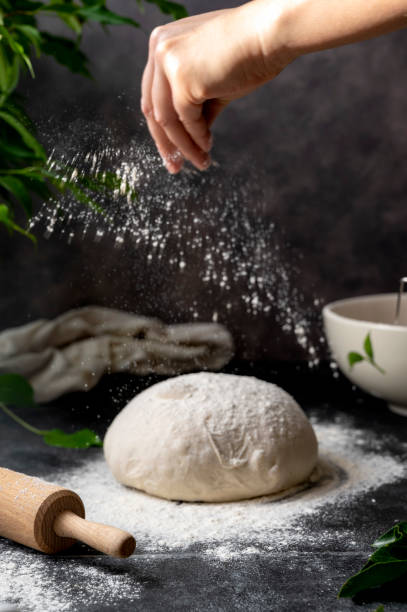 istock Cooking sourdough homemade bread. Sieving flour over raw bread dough on table, dark background, selective focus. 1368060931