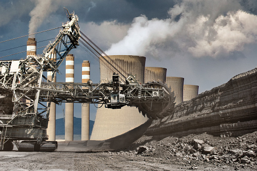 Wheel Bucket Excavator Working At Coal Mines with coal-fired power station in background.