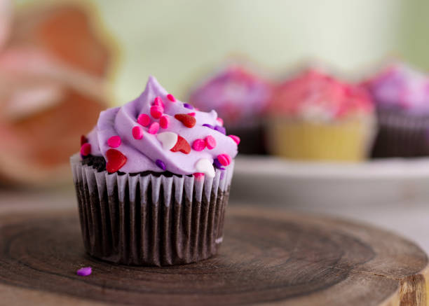 un cupcake di san valentino al cioccolato su una lastra di legno e tulipani e cupcake aggiuntivi sfocati sullo sfondo. - little cakes foto e immagini stock