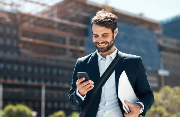 Photo of Shot of a young businessman using a smartphone against an urban background