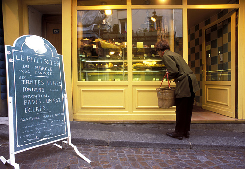 Shopper browsing in front of bright Patisserie façade, Rue Mouffetard, Latin Quarter, Paris, France. As capital city of France, Paris offers architecture,design, art and culture that spans many cultures and eras, often defined by the landmarks that remain today to mark the milestones of French life and history.