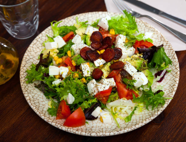Refreshing salad with greens, tomatoes, avocado, corn, mozzarella and fried sausages
