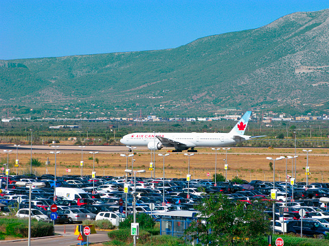 Athens, Greece - September 24, 2021: Air Canada airplane at the Athens International Airport Eleftheros Venizelos. There are many cars in the airport parking lot. Airplane on the runway against the backdrop of mountains.