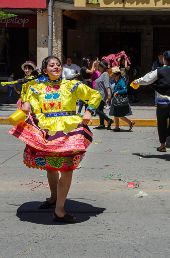 Huaraz, Peru - February 2020: A woman dancing during carnival parade in Huaraz city. Girl with braids wears a yellow and red dress with traditional Peruvian embroidery. Cheerful celebration