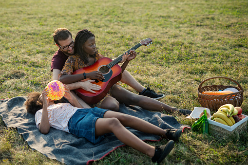 Happy diverse family having fun and playing guitar on picnic