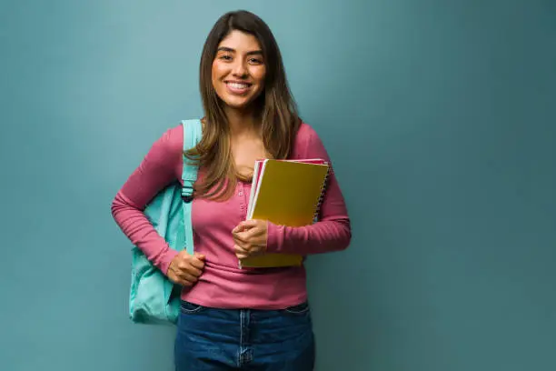 Happy young woman wearing a backpack while carrying books and notebooks to college