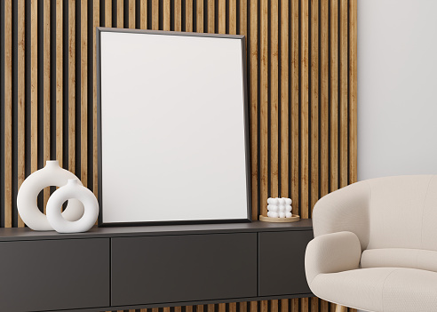 Empty vertical picture frame on wooden wall in modern living room. Mock up interior in contemporary style. Free space for picture, poster. Console, armchair, vase, candle. 3D rendering