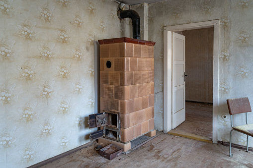 An old tiled stove in an apartment room in East Germany. Abandoned place inside of an ancient building. Vintage interior design of a weathered empty home in a bad condition.