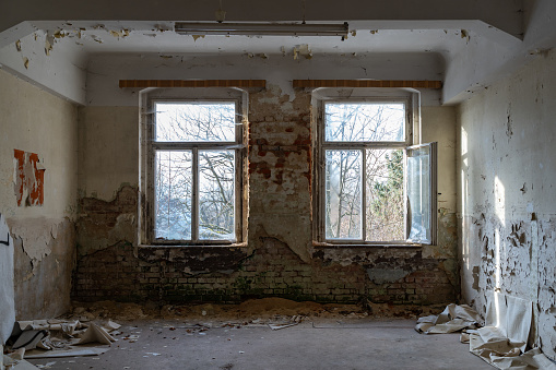 Viewing in an old room with big windows. Empty place in an abandoned building. Bricks come through the wall plaster and paint is peeling off. Ruined apartment in bad condition.