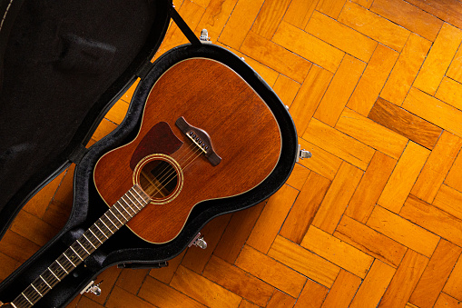 Directly above photo of a wooden guitar inside a case on a wooden floor with copy space in the right side