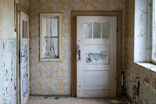 Old door and window in an abandoned building. Background scene of a vintage interior space with wallpaper. Paint is peeling off the walls and a lot of dirt is lying around.