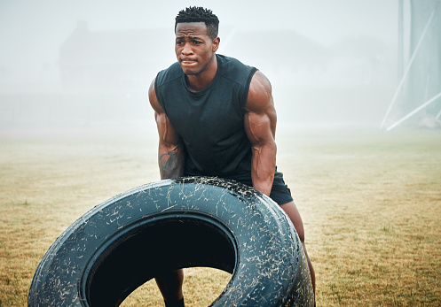 Shot of a muscular young man flipping a tyre while exercising outdoors