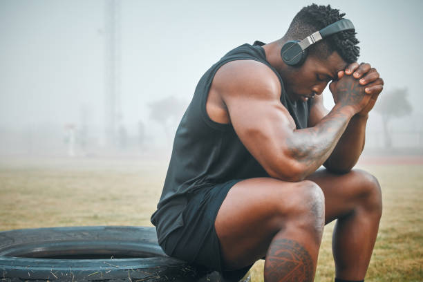 photo d’un jeune homme musclé portant des écouteurs alors qu’il faisait de l’exercice à l’extérieur - tired men african descent sadness photos et images de collection