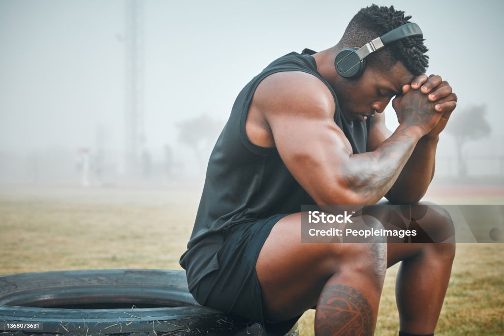 Shot of a muscular young man wearing headphones while exercising outdoors I'll just have to keep working harder Athlete Stock Photo