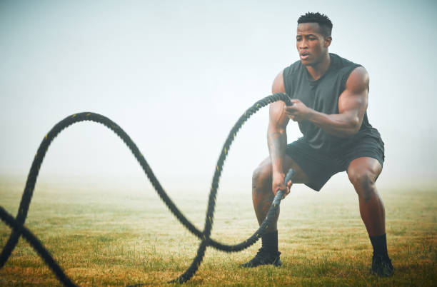 photo d’un jeune homme musclé s’entraînant avec des cordes de combat à l’extérieur - men weight training african descent male photos et images de collection