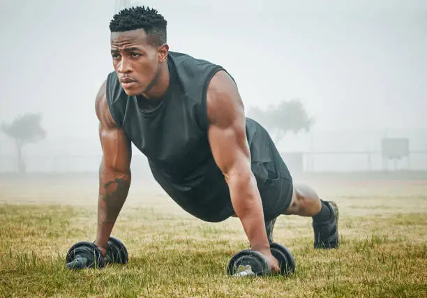 Photo of Shot of a muscular young man exercising with dumbbells outdoors