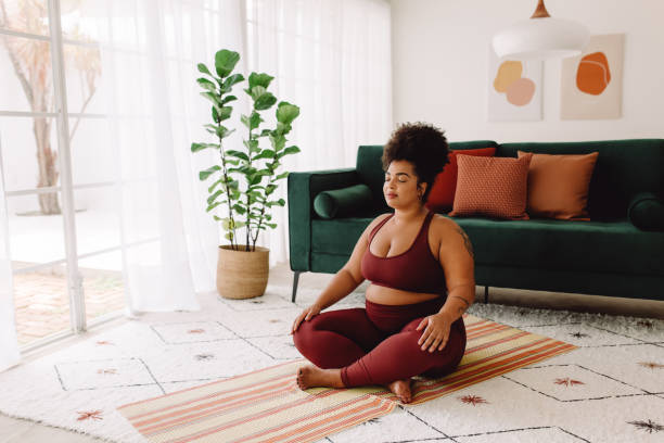 Plus size woman practicing meditation at home Body positive woman doing mindfulness workout at home. Beautiful female in sports wear practicing meditation at home. meditating stock pictures, royalty-free photos & images
