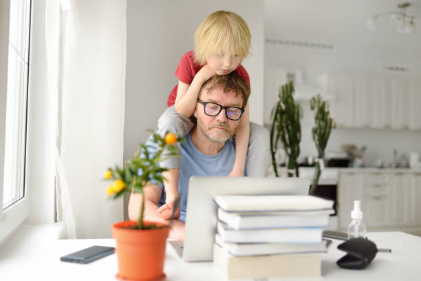 istock Man is working from home with laptop during quarantine. Home office and parenthood at same time. Exhausted parent with hyperactive child. 1368075117