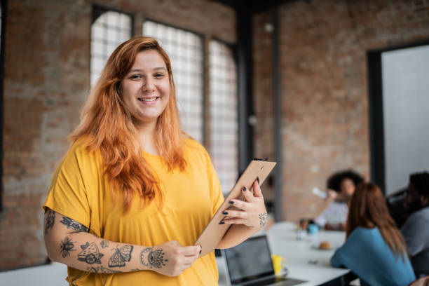 portrait of a young business woman holding a clipboard in an office - portrait tattoo photography color image imagens e fotografias de stock