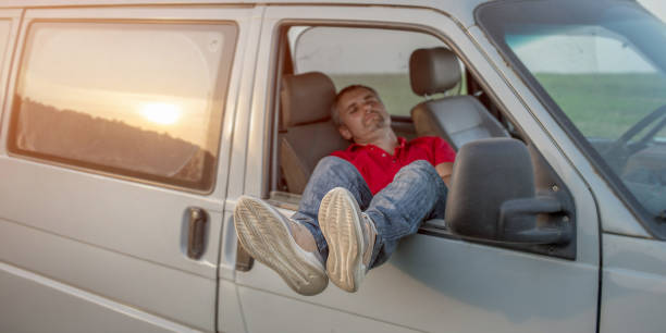 Tired driver sleeping inside of vehicle stretching legs out open side window