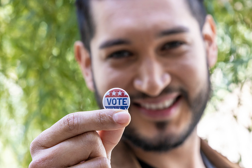 A young hispanic adult male holding a voting badge