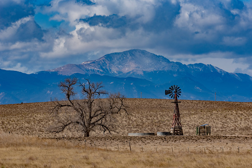 Two rut dirt wagon/truck trail leads to an old windmill with Pikes Peak in background. This is looking west from prairie land of El Paso County on the outskirts of Colorado Springs, Colorado in western United States of America (USA).