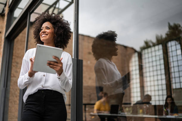 Businesswoman looking away and using digital tablet in an office Businesswoman looking away and using digital tablet in an office forecasting stock pictures, royalty-free photos & images