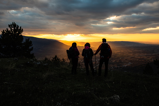 A group of hikers is admiring the sunset from the top of a hill