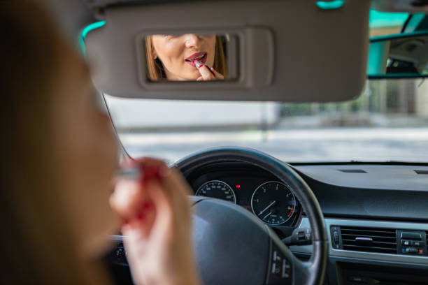 Young elegant woman looking in the car view mirror while applying lipstick stock photo