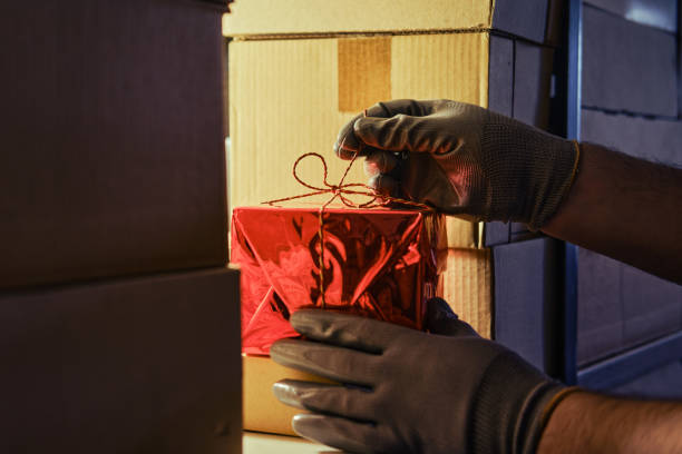 手袋をした男の手は、クリスマスと大晦日に店の倉庫でギフトボックスを取ります。ギフト商品の配達時の盗難の問題 - christmas stack gift carrying ストックフォトと画像