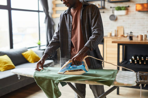 Man Ironing Clothes Cropped shot of young African-American man ironing clothes in studio apartment, bachelor lifestyle and household chores concept, copy space iron laundry cleaning ironing board stock pictures, royalty-free photos & images