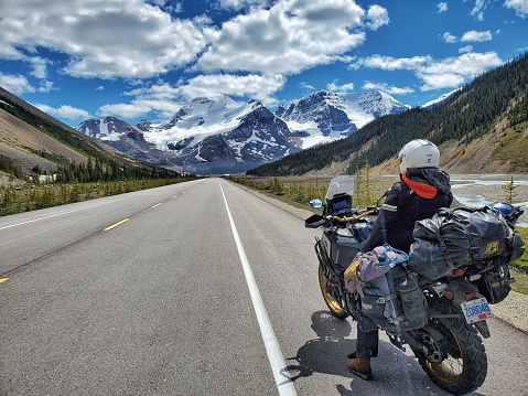 A person sits on a motorcycle looking South, towards Mt Athabasca, a mountain at the Columbia Ice Fields, on the Icefields Parkway, in Jasper Nati Park, Alberta, Canada.