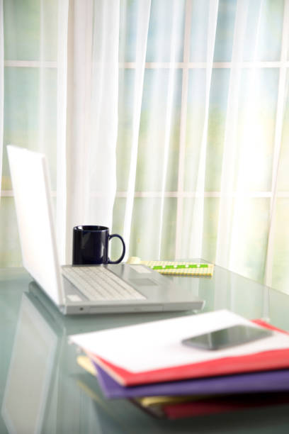istock LV Lap top computer on glass top desk.  Stack of file folders in foreground.  Coffee cup and notepad on far side of laptop. 1368093819
