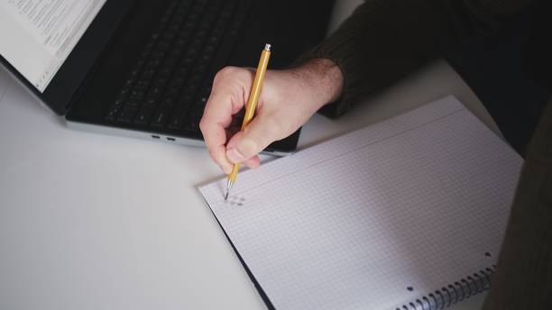 istock Caucasian Male Procrastinating Drawing Abstract Shapes in Square Ruled Notebook with Mechanical Pencil during Boring Meeting 1368093934