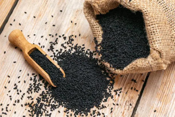 Black cumin seeds and wooden scoop, texture background.