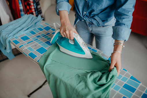 Young female adult ironing the laundry at home in the living room.