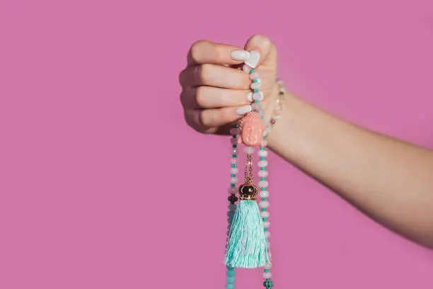 Woman lit hand counts mala beads strands of gemstones used for keeping count during mantra meditations. Pink background. Spirituality, religion, God concept. High quality photo