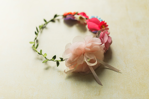 Close up shot of a cute girly headband with colorful roses, flowers and leaves, lying on a pastel yellow background.
