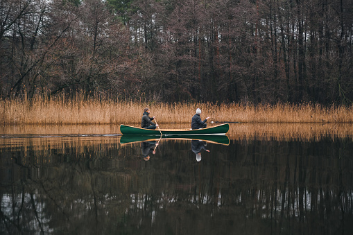 Two men paddling a beautiful green canoe on the river. Spring or autumn scene with a wooden boat on calm water