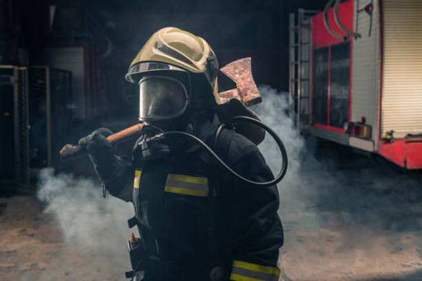 救助斧を持つ消防士の投票率を身に着けている消防士の肖像画。煙と青い光と暗い背景。 - turnouts ストックフォトと画像
